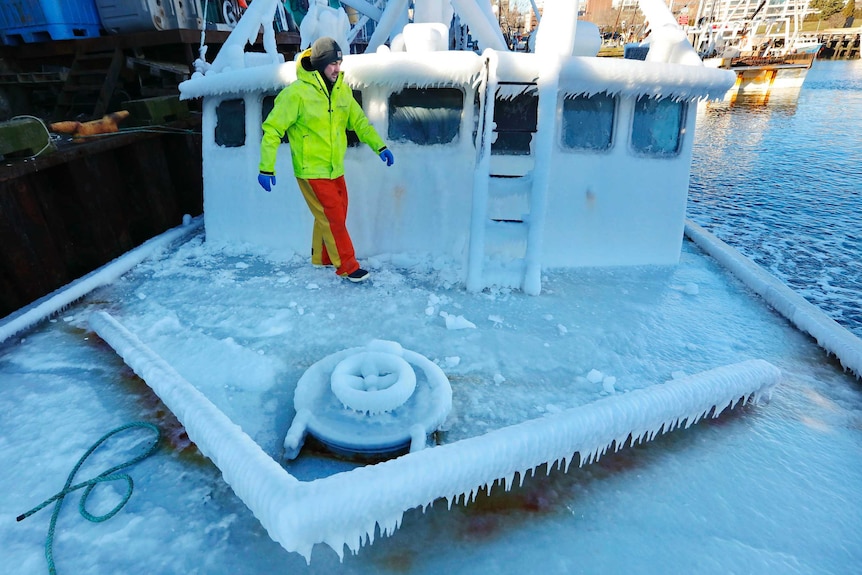 A man walks across the top a lobster boat which is covered in ice in a Massachusetts harbour.