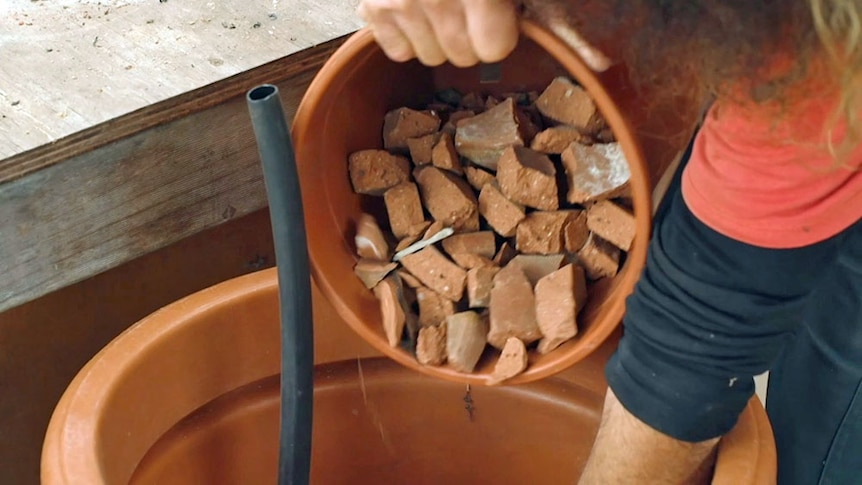 Crushed terracotta being pored into a large plastic pot.