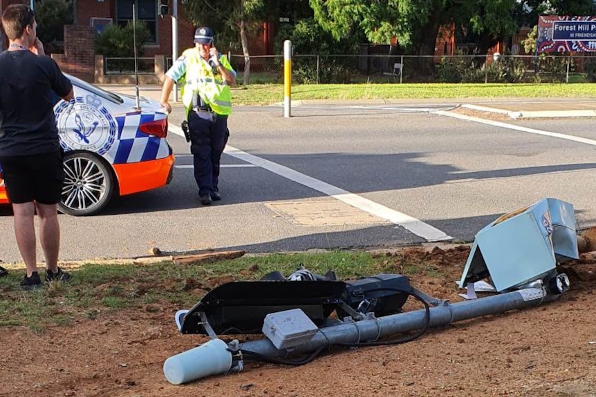 Traffic light on its side, police vehicle in background on busy road.