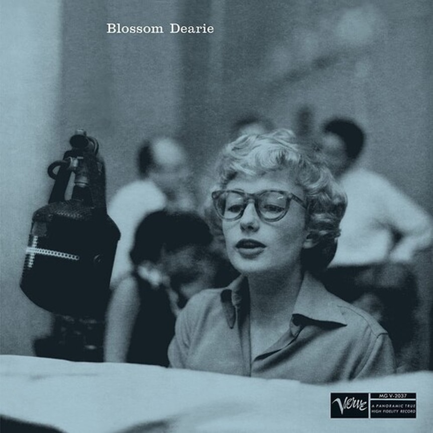 A monochrome photo of pianist Blossom Dearie at the keyboard and singing into a large microphone