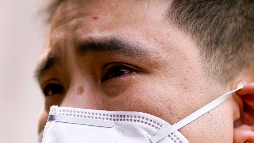 A close up of a man's face in a surgical mask with tears rolling down his cheeks