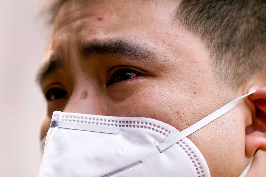 A close up of a man's face in a surgical mask with tears rolling down his cheeks