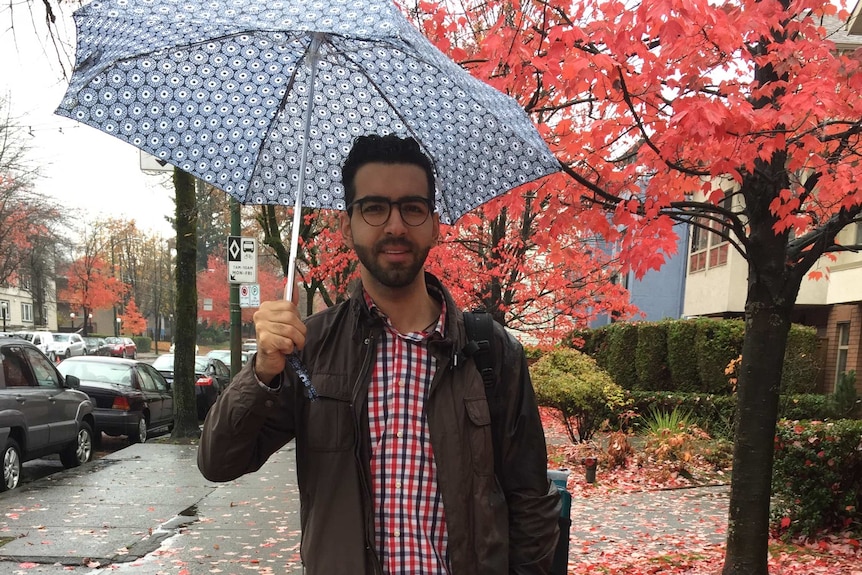 A man with an umbrella stands on a footpath.