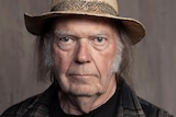 Headshot of Neil Young looking at the camera wearing a straw broad-brimmed hat and checked shirt
