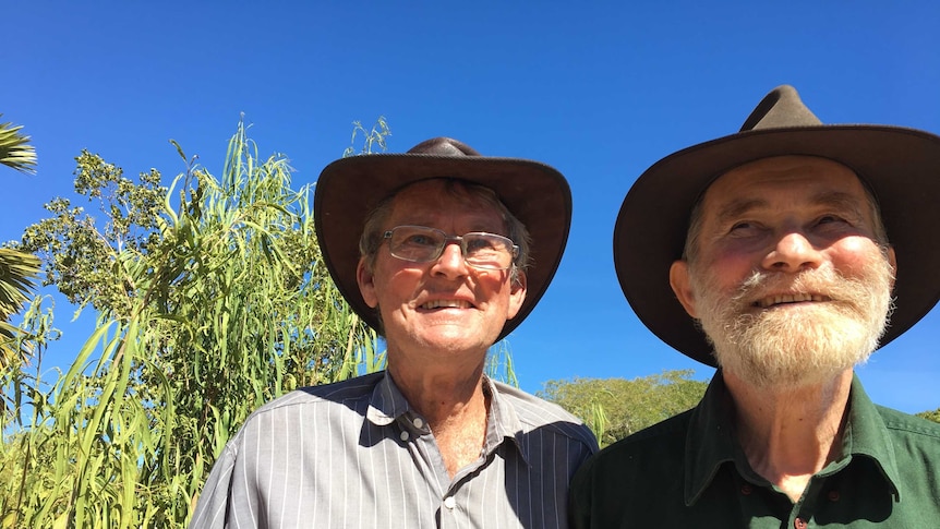 Two men with bush hats smile in the sunshine and blue sky