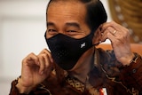 The Indonesian president smiles as he begins to take off his face mask.