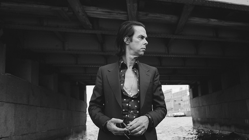 Black and white image of Nick Cave holding sunglasses