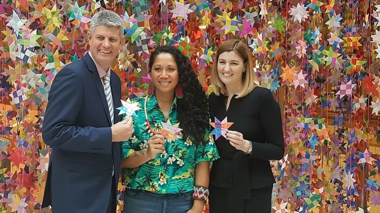 A man and two women stand in front of a large display of ribbon stars