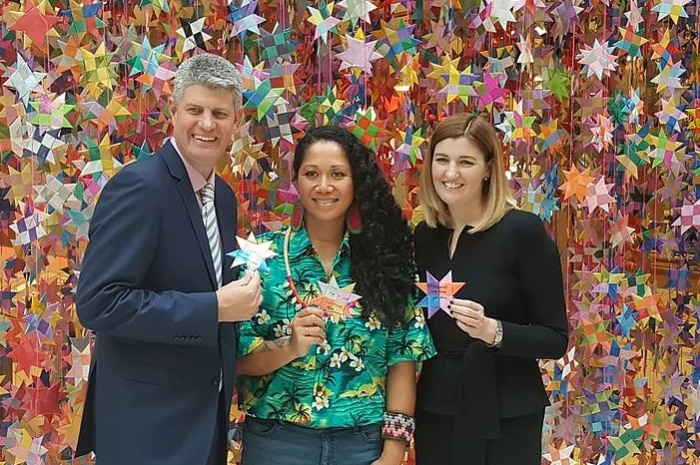 A man and two women stand in front of a large display of ribbon stars