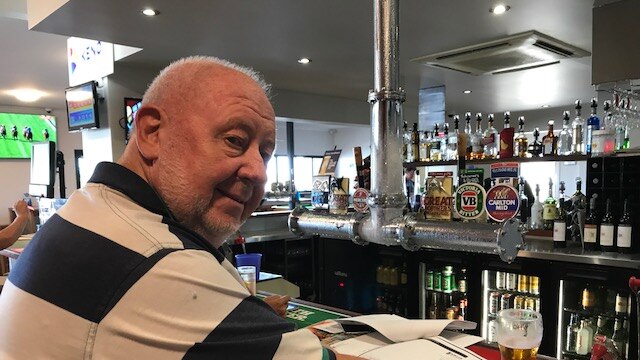 Bruce Hedditch sits at the bar in a pub with papers and a beer in front of him