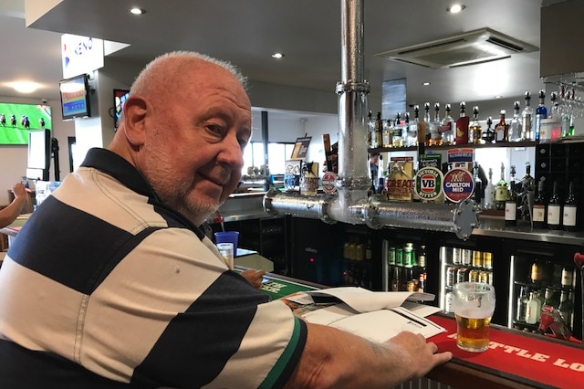 Bruce Hedditch sits at the bar in a pub with papers and a beer in front of him