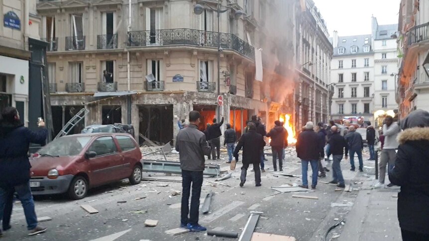 Witnesses congregate on a traditional Parisian street as the ground floor of a bakery burns.