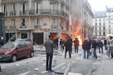 Witnesses congregate on a traditional Parisian street as the ground floor of a bakery burns.