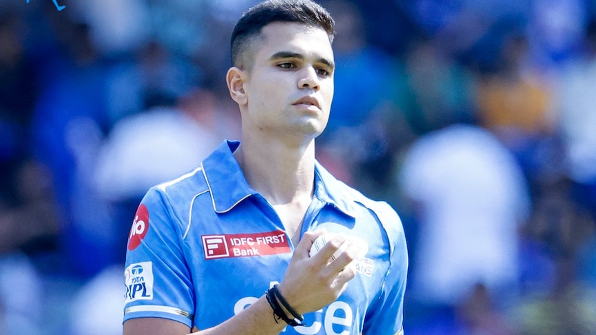 Arjun Tendulkar holds a white cricket ball while wearing the blue jersey of Mumbai Indians in the Indian Premier League.