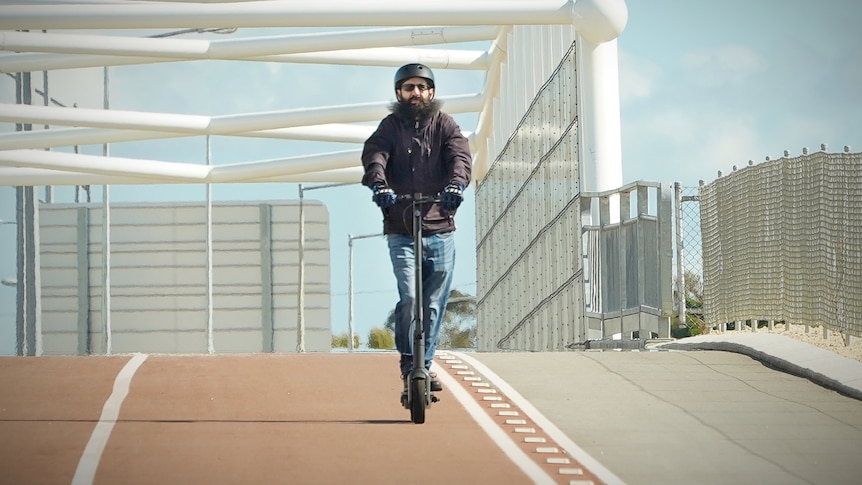 A bearded man rides an e-scooter on an orange brown bike path