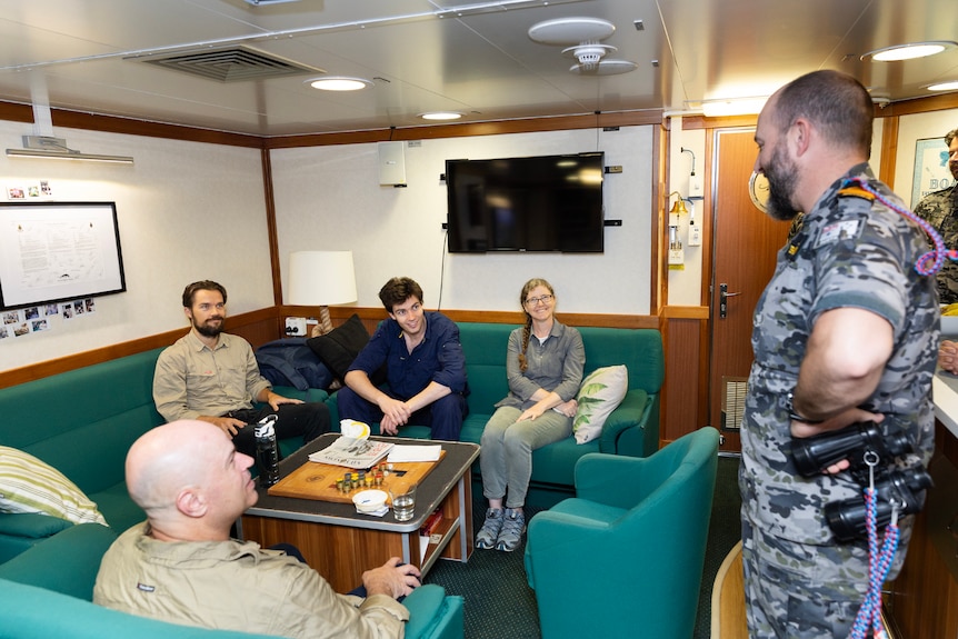 Four people sit on a couch while talking to a man in a Navy uniform