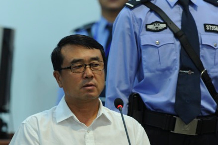 A Chinese man in a white shirt sits behind a standing police officer