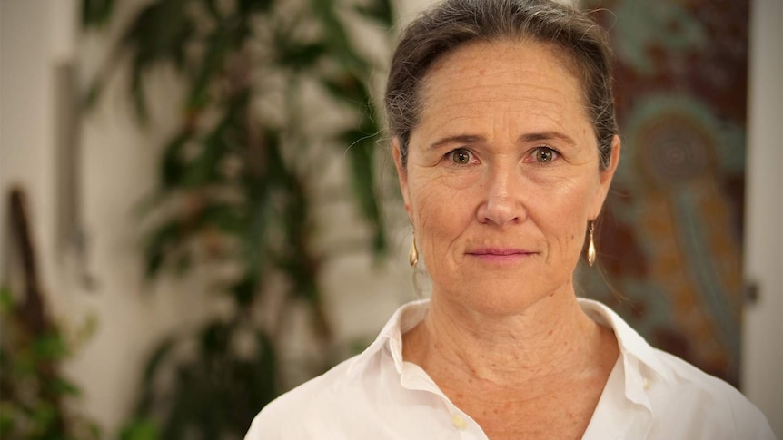 Sally Stevenson standing in a room inside Centre with a determined look on her face. There are blurred green plants behind her