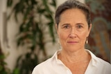 Sally Stevenson standing in a room inside Centre with a determined look on her face. There are blurred green plants behind her