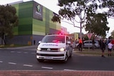 A police van is parked outside a shopping centre with a number of people nearby including children sitting on a curb.