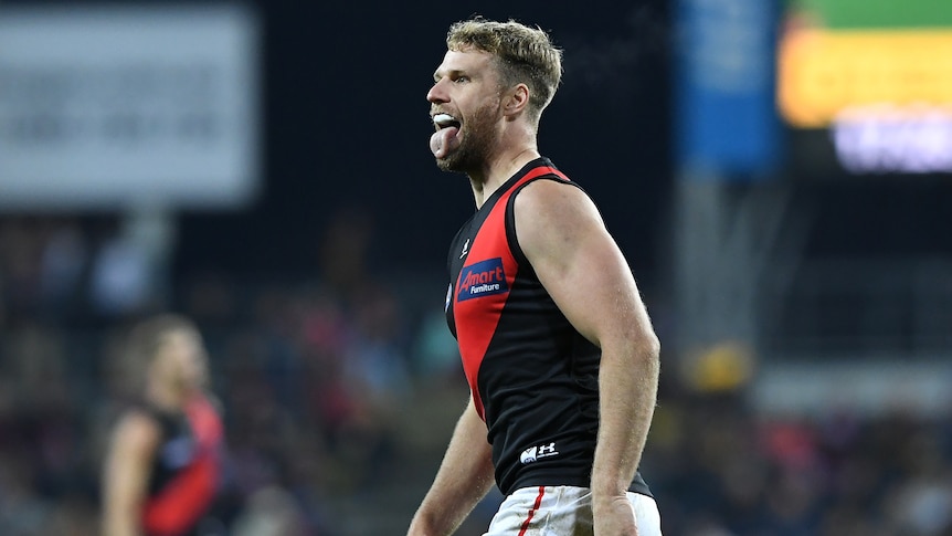 An Essendon AFL player makes an expression with his face after kicking a goal against Hawthorn.