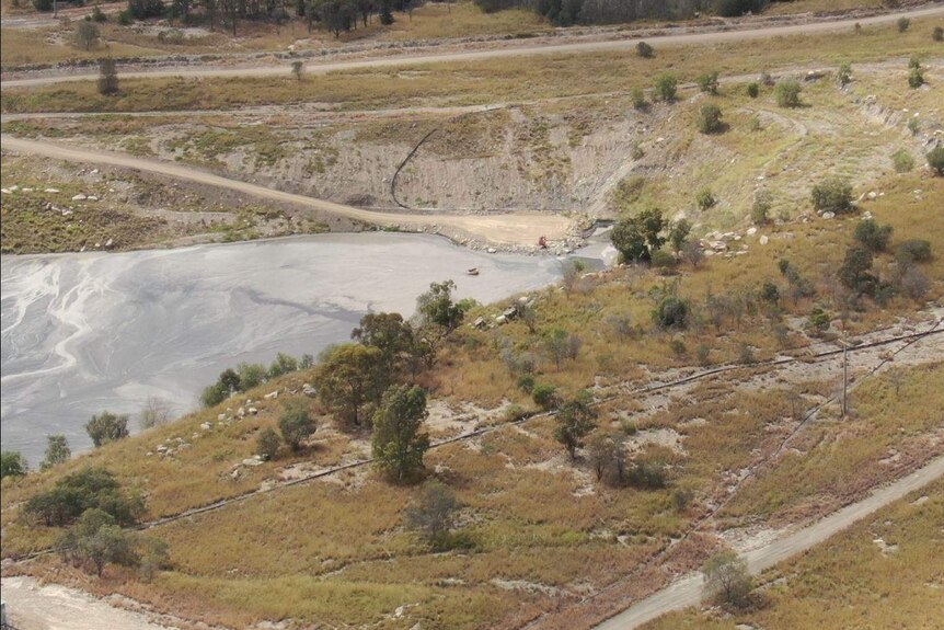An aerial shot of a black pipe that end in a large grey ash dam.