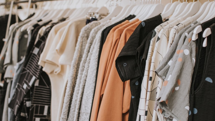 Clothing hung on white hangers on a metal rack.