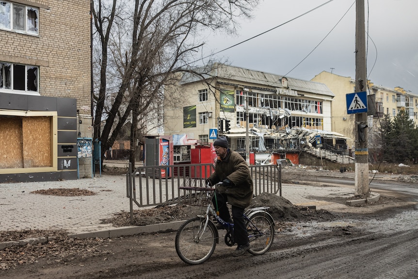 a person rides a bike past damaged buildings in Bakhmut during the day time