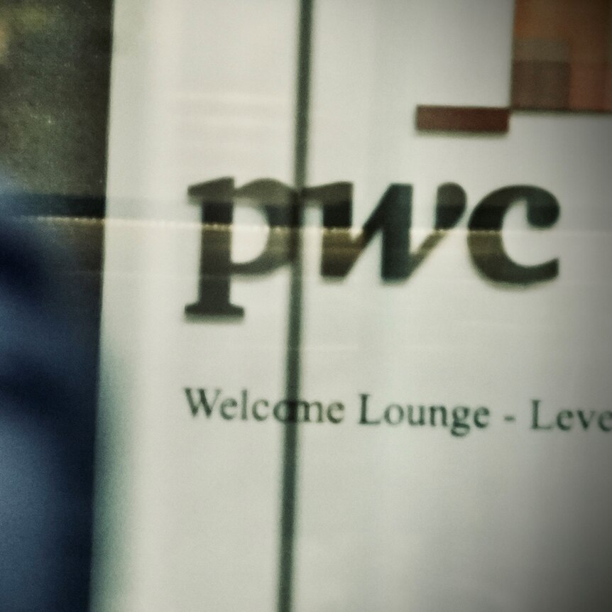 A person's blurred shoulder as they walk past a PWC logo.