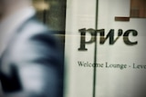A person's blurred shoulder as they walk past a PWC logo.