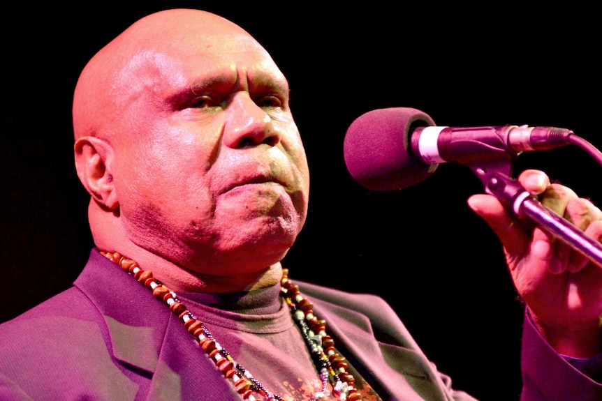 Close up on Archie Roach singing into a microphone.