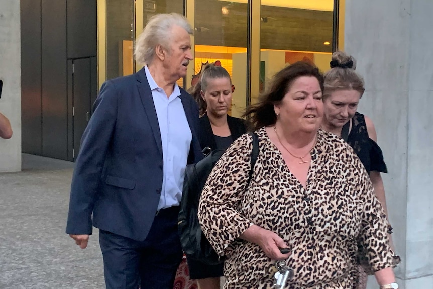 A young woman in light hair and a black suit leaves a building surrounded by two women and one man.