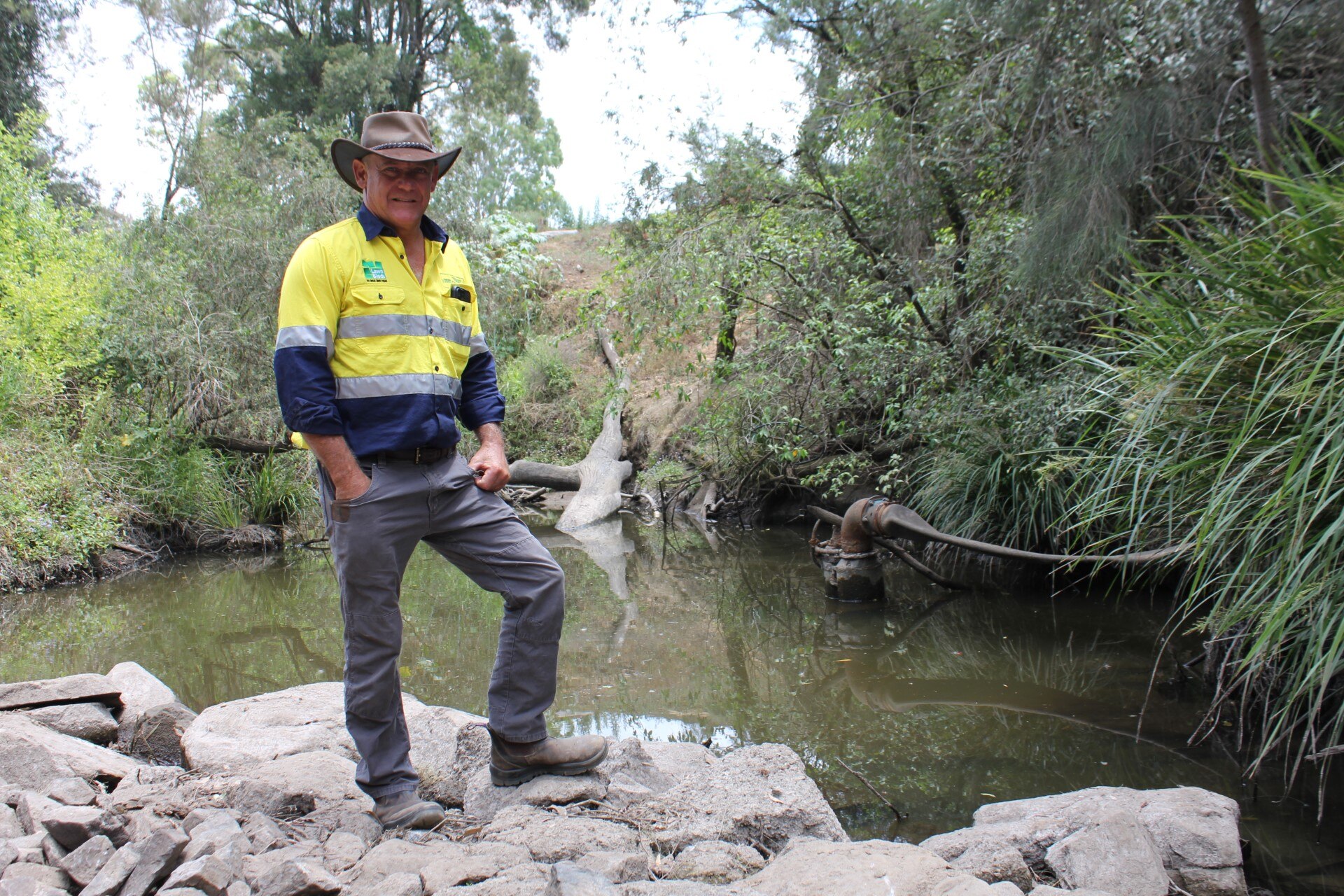 Man standing near creek with pump