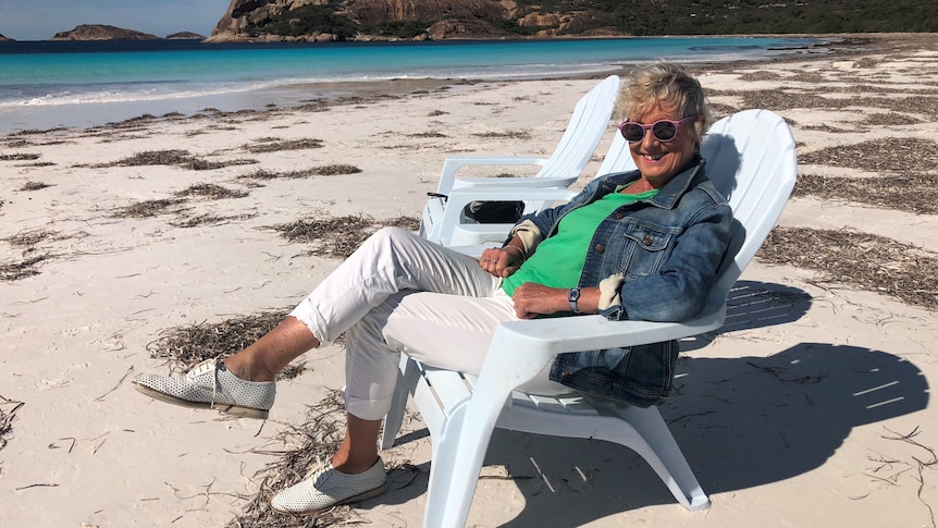 Heather Ewart sits in a white chair on the sand.