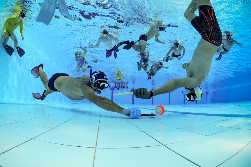 two underwater hockey players vy for the puck.