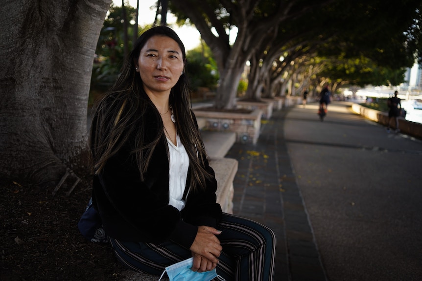 A woman sits with her hands folded on a park bench