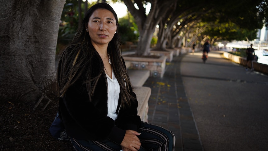 A woman sits with her hands folded on a park bench