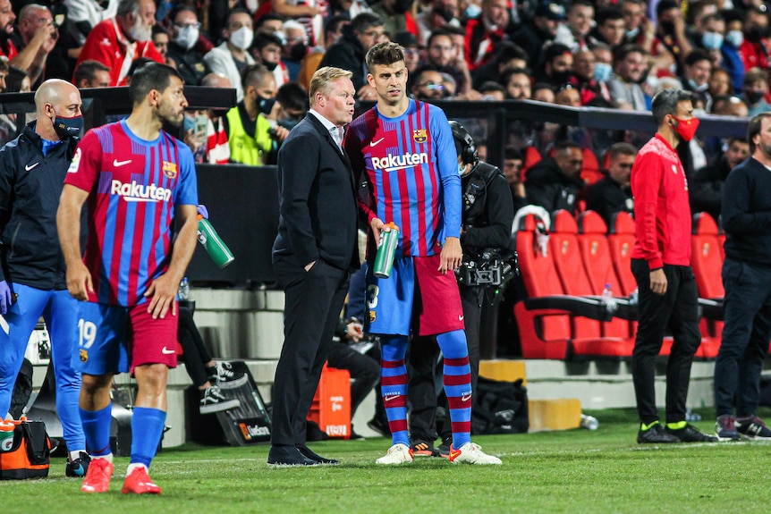 Ronald Koeman speaks to Gerard Pique while standing in front of the bench