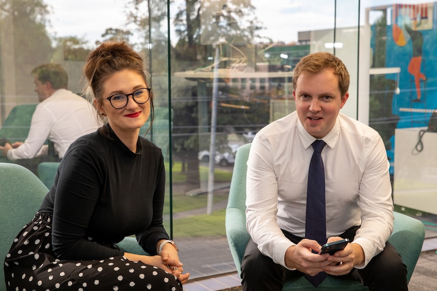 Kirsti Taylor and her boss John de la Motte sit in chairs in front of a window looking out onto trees.