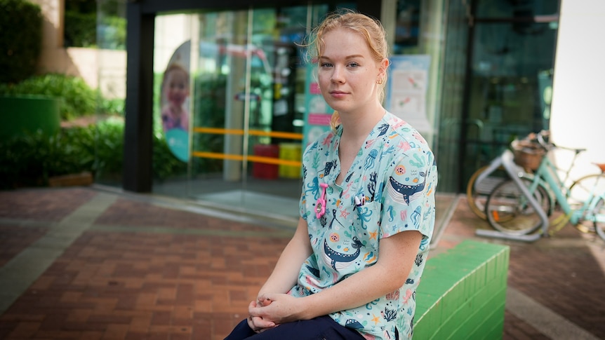 Victoria sits outside a hospital, wearing colourful scrubs printed with pictures of whales and other sea life.