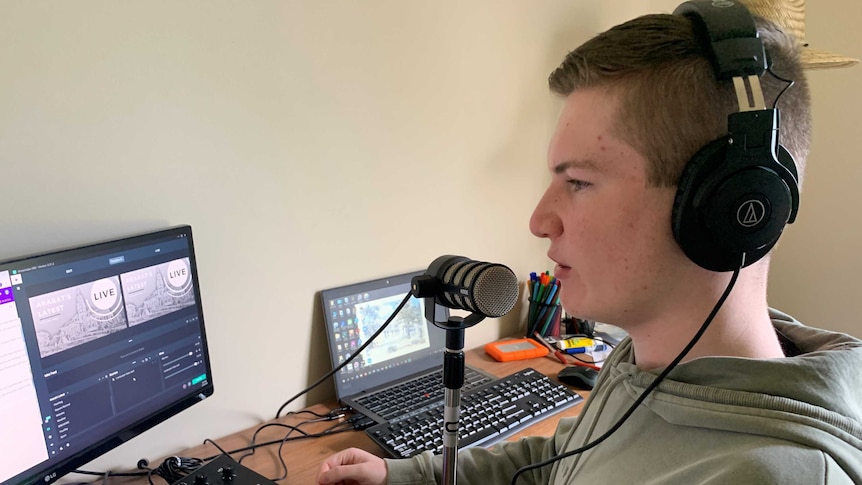 A teenage boy wearing headphones sits in front of a microphone and recording equipment.