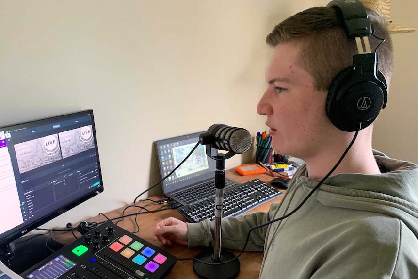 A teenage boy wearing headphones sits in front of a microphone and recording equipment.