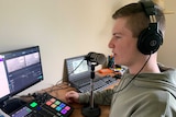 A teenage boy wearing headphones sits in front of a microphone and recording equipment.