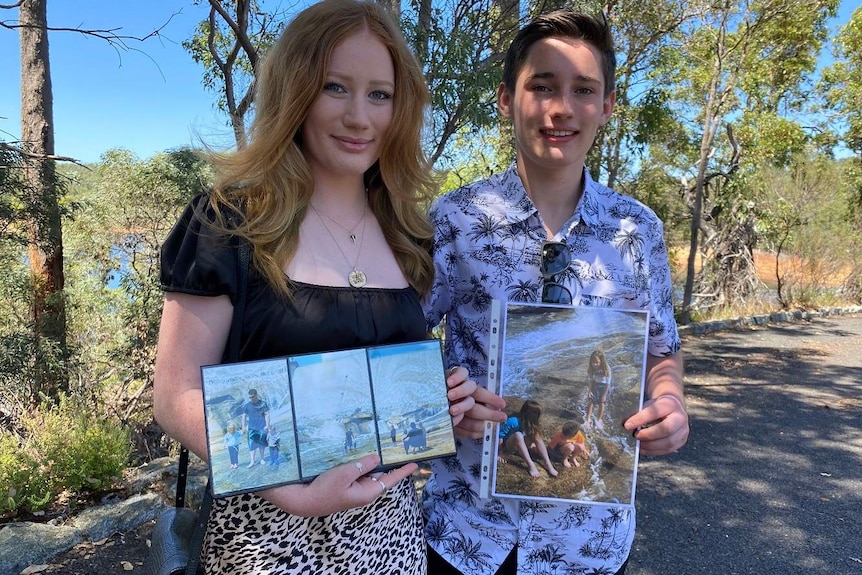 A teenage boy and girl holding photos of people at a dam