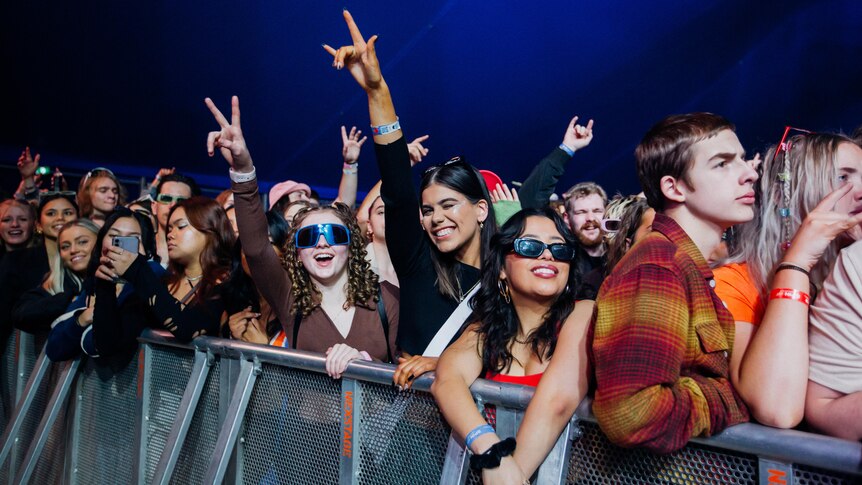 A photo of festival attendees on the barrier smiling and posing while wearing sunglasses.