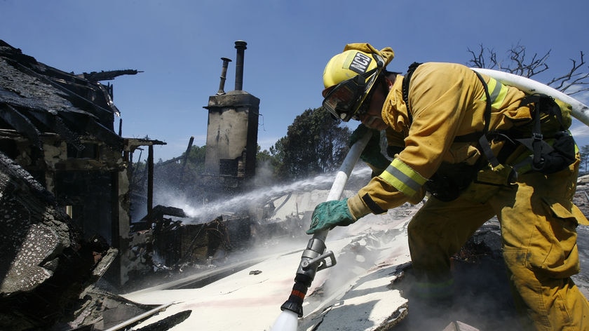 A firefighter sprays water on the rubble of a house