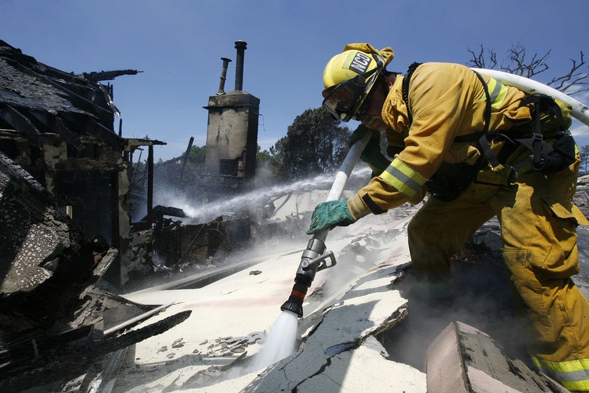 A firefighter sprays water on the rubble of a house
