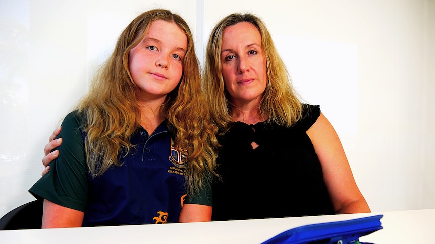 teenage daughter and mother sit at a kitchen table 
