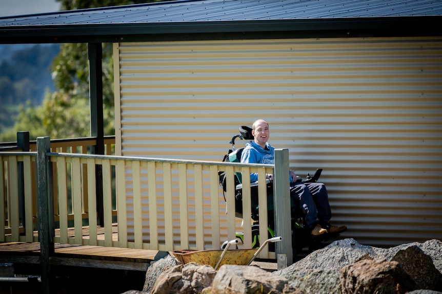 Nathan smiling widely as he travels down the verandah alongside the corrugated iron wall of his house.