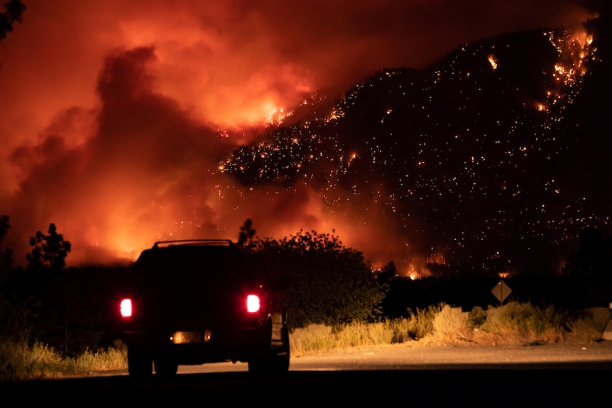 A four-wheel drive vehicle is parked on the road in front of a forest on fire.